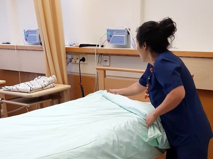 Kuvassa laitoshuoltaja vaihtaa sairaalan sänkyyn uudet vuodevaatteet